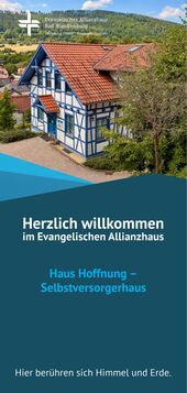 Ein traditionelles, zweigeschossiges Fachwerkhaus mit rotem Dach und weißen Wänden, umgeben von grüner Landschaft. Ein Willkommensschild weist auf das Evangelische Allianzhaus und das Selbstversorgerhaus "Haus Hoffnung" hin. (Text KI generiert)